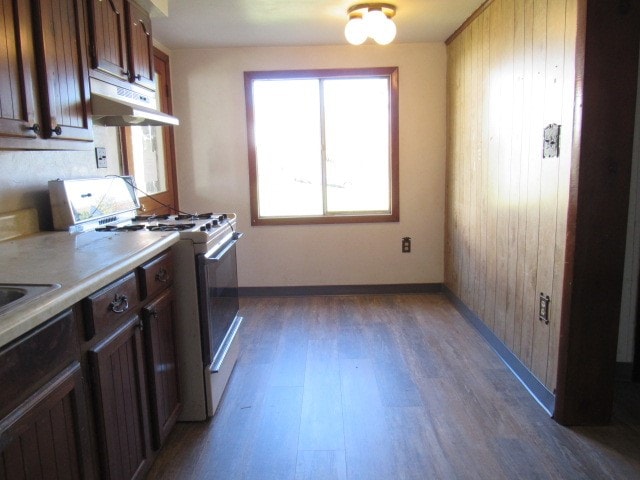 kitchen featuring dark wood-type flooring, wooden walls, and white range with gas stovetop