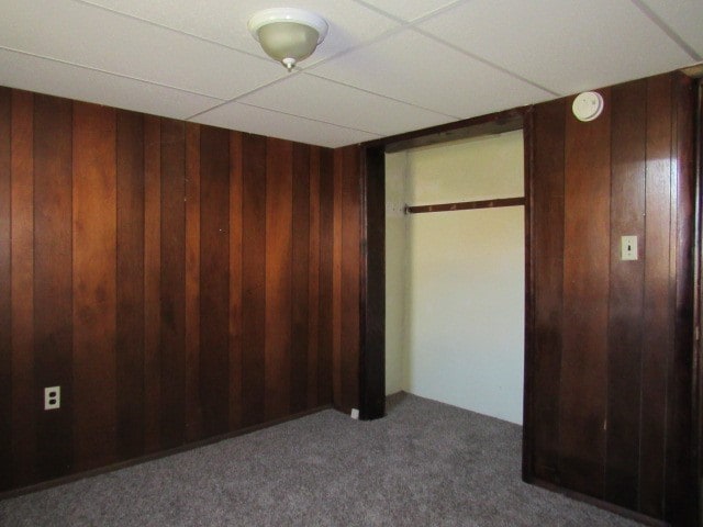 unfurnished bedroom featuring a drop ceiling, carpet, wood walls, and a closet