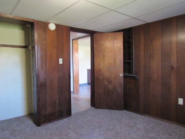 unfurnished bedroom with wood walls, a closet, carpet, and a drop ceiling