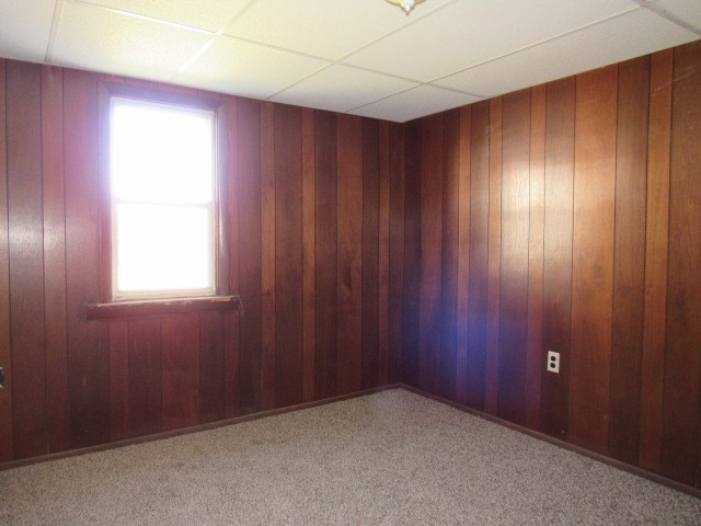 empty room featuring a paneled ceiling, wooden walls, and light carpet