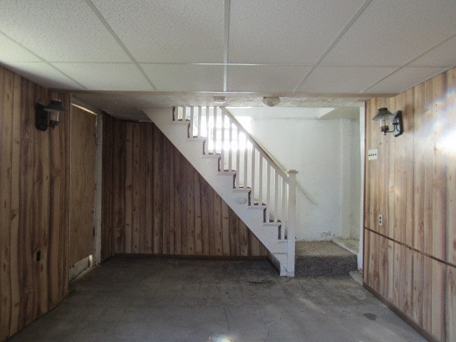 basement featuring a paneled ceiling and wooden walls