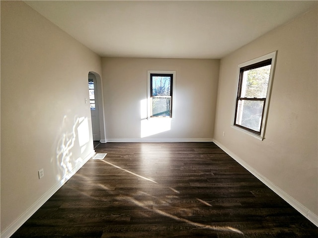 empty room with a wealth of natural light and dark hardwood / wood-style floors