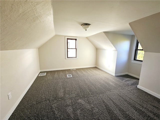 additional living space with a wealth of natural light, lofted ceiling, and dark carpet