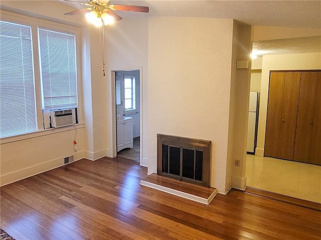 unfurnished living room featuring a ceiling fan, wood finished floors, a fireplace with raised hearth, cooling unit, and baseboards