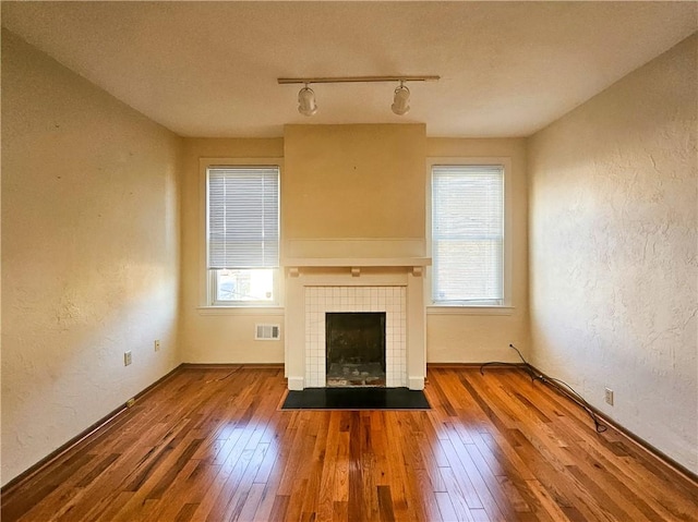 unfurnished living room featuring a textured wall, hardwood / wood-style floors, track lighting, plenty of natural light, and a fireplace