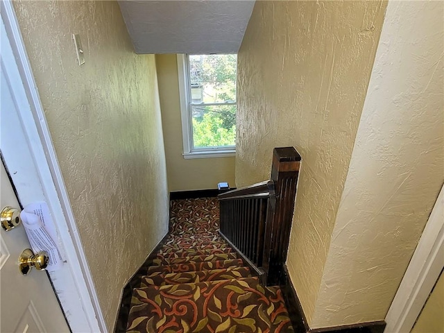 hallway featuring an upstairs landing and a textured wall