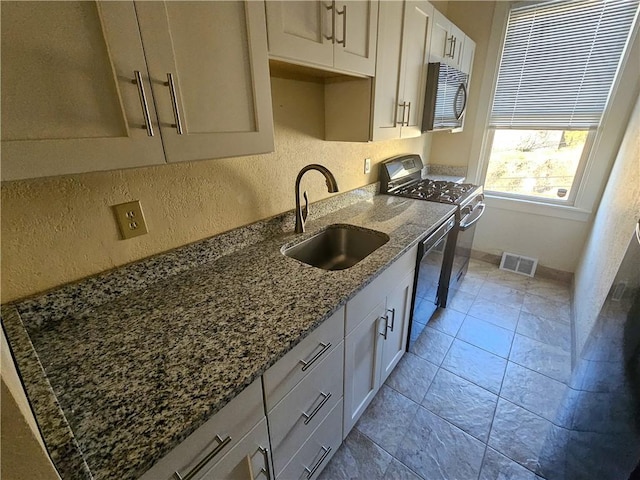 kitchen with stainless steel microwave, a sink, range with gas cooktop, dishwashing machine, and dark stone countertops