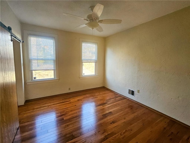 spare room featuring wood-type flooring, a barn door, a textured wall, and ceiling fan