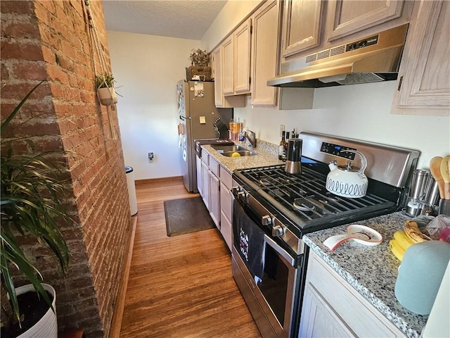 kitchen with stainless steel appliances, under cabinet range hood, light wood-style floors, a textured ceiling, and a sink