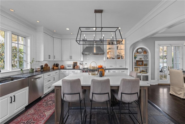 kitchen featuring a center island, white cabinets, wall chimney range hood, stainless steel dishwasher, and dark hardwood / wood-style flooring