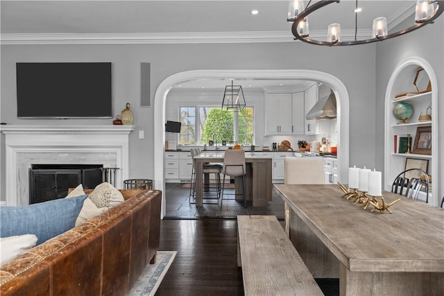 dining room with built in shelves, dark wood-type flooring, a premium fireplace, crown molding, and a chandelier