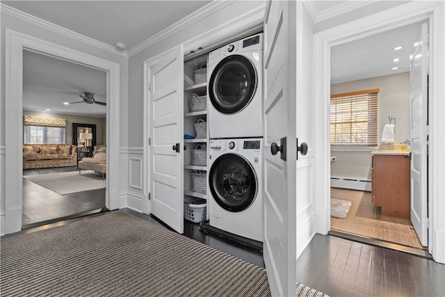 laundry room featuring dark hardwood / wood-style flooring, stacked washing maching and dryer, ornamental molding, baseboard heating, and ceiling fan