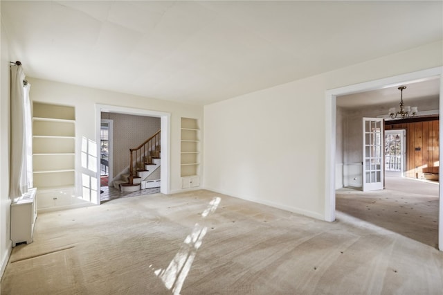 spare room with light carpet, built in shelves, an inviting chandelier, and french doors