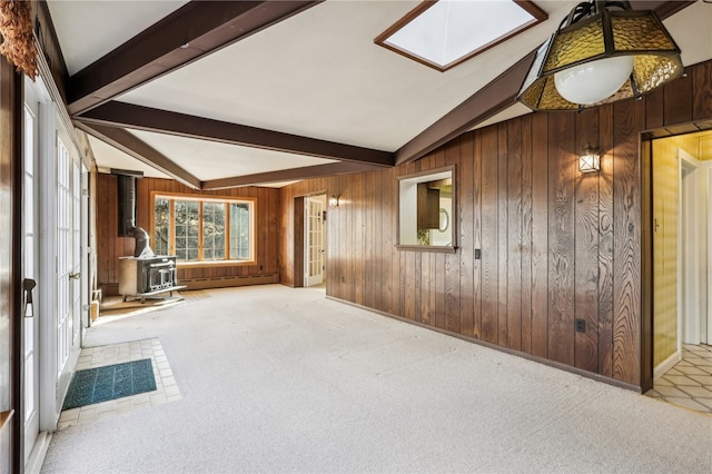 unfurnished living room with carpet, lofted ceiling with skylight, a wood stove, a baseboard heating unit, and wooden walls