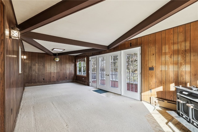 unfurnished living room featuring vaulted ceiling with beams, light carpet, wooden walls, and french doors