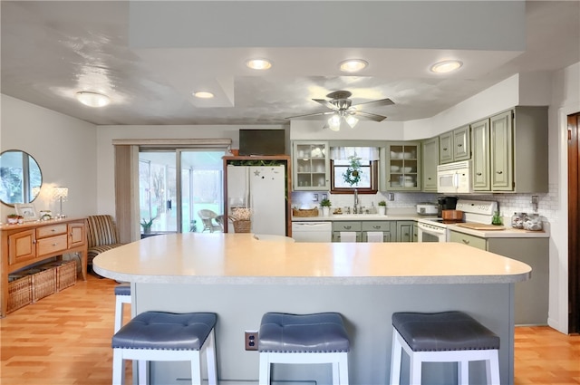 kitchen with decorative backsplash, a breakfast bar, light hardwood / wood-style floors, and white appliances