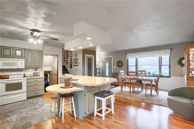 kitchen featuring light hardwood / wood-style floors, a kitchen breakfast bar, green cabinets, and white appliances