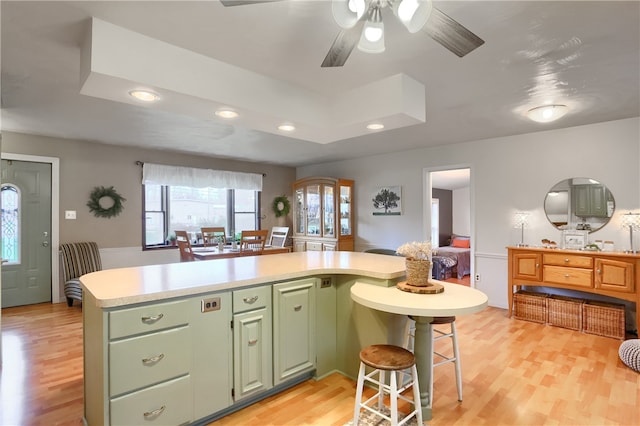 kitchen featuring a breakfast bar, ceiling fan, light wood-type flooring, and green cabinetry