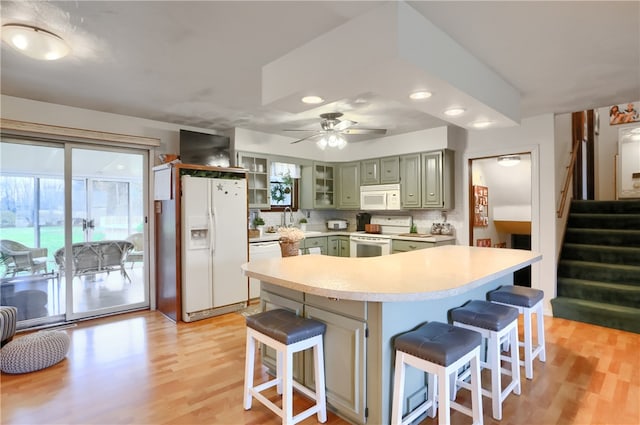 kitchen featuring decorative backsplash, a kitchen breakfast bar, light wood-type flooring, white appliances, and green cabinetry