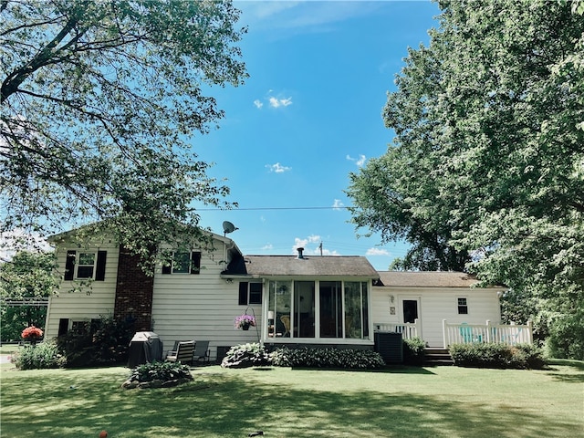 rear view of house featuring a lawn, a sunroom, and a deck