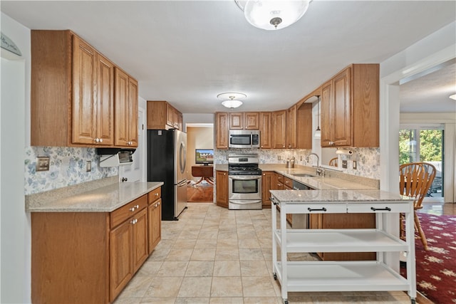 kitchen featuring kitchen peninsula, light stone countertops, tasteful backsplash, stainless steel appliances, and sink