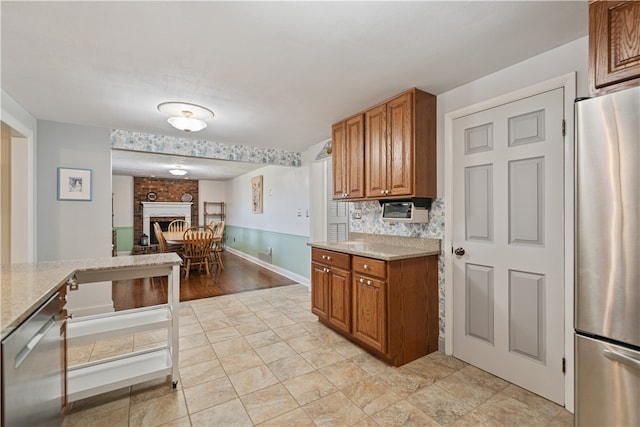 kitchen with decorative backsplash, light stone countertops, stainless steel appliances, and a brick fireplace