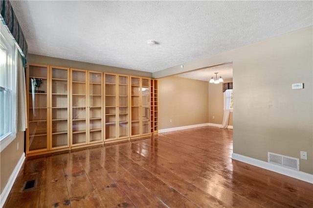 spare room featuring an inviting chandelier, dark hardwood / wood-style floors, and a textured ceiling