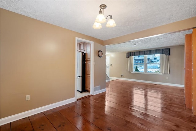 spare room featuring wood-type flooring, a chandelier, and a textured ceiling