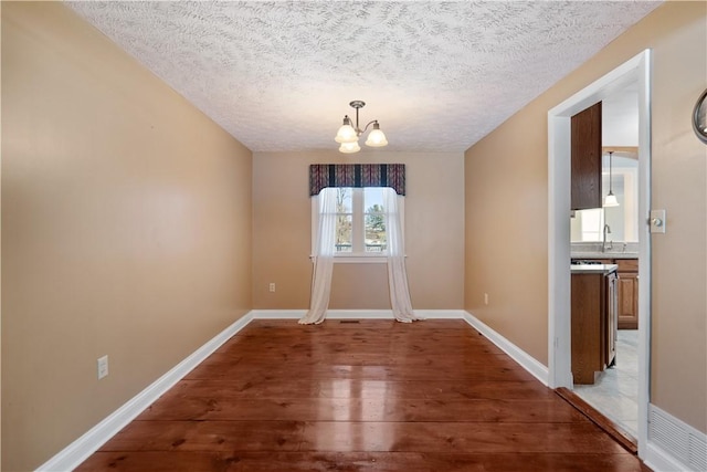 unfurnished dining area featuring an inviting chandelier, sink, hardwood / wood-style floors, and a textured ceiling