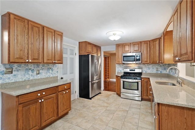 kitchen with stainless steel appliances, light stone countertops, sink, and backsplash