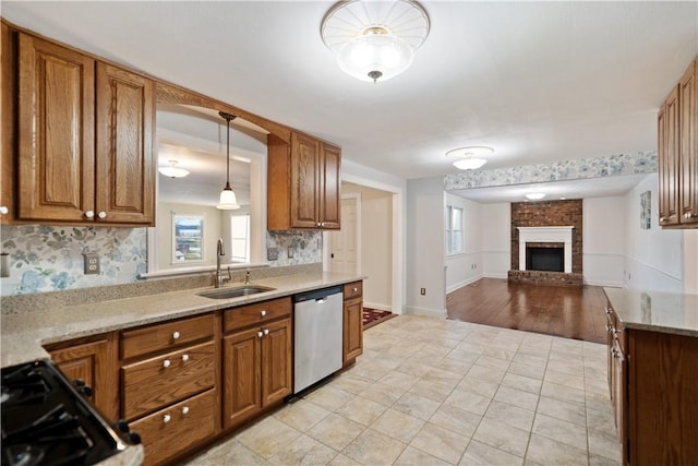 kitchen featuring sink, hanging light fixtures, tasteful backsplash, a brick fireplace, and stainless steel dishwasher