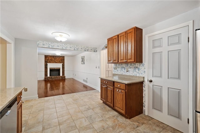 kitchen featuring light stone counters, a brick fireplace, backsplash, and stainless steel dishwasher