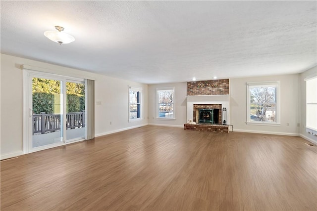 unfurnished living room with hardwood / wood-style floors, a textured ceiling, a wealth of natural light, and a brick fireplace