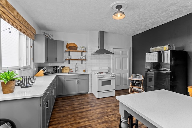 kitchen featuring white gas stove, sink, black refrigerator, dark hardwood / wood-style floors, and wall chimney range hood