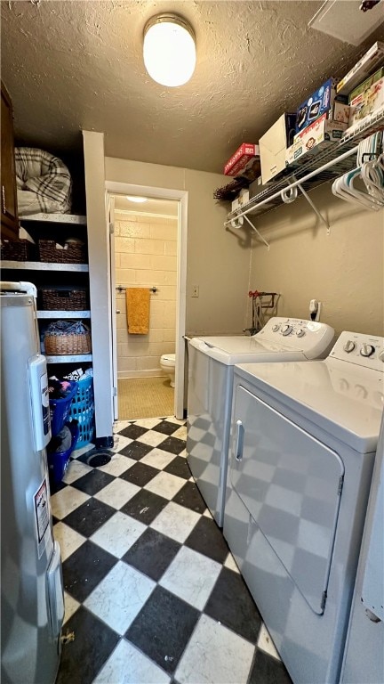 clothes washing area featuring a textured ceiling, electric water heater, and washing machine and clothes dryer