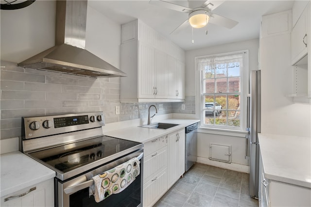 kitchen with wall chimney range hood, appliances with stainless steel finishes, sink, and white cabinets