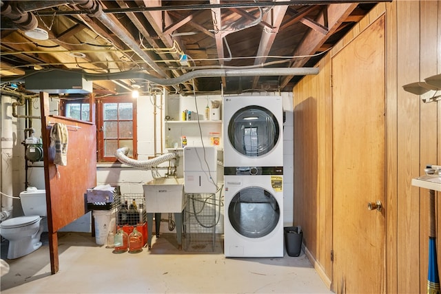 clothes washing area featuring wood walls, stacked washer and dryer, and sink