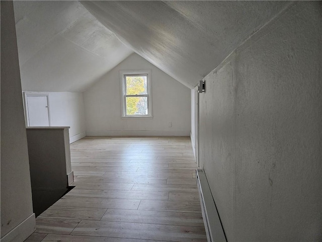 additional living space with light wood-type flooring, a textured ceiling, lofted ceiling, and a baseboard heating unit