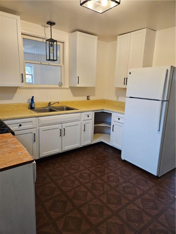 kitchen featuring white fridge, wood counters, white cabinetry, hanging light fixtures, and sink