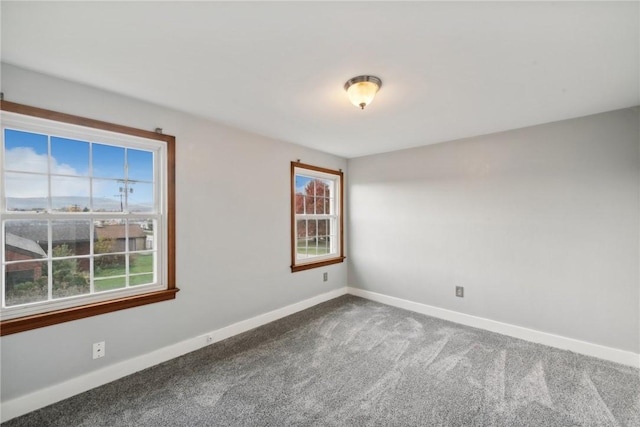 unfurnished room featuring healthy amount of natural light, baseboards, and dark carpet