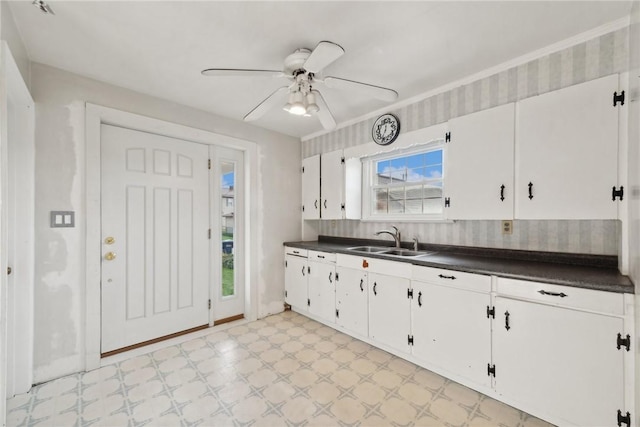 kitchen featuring light floors, a sink, dark countertops, a ceiling fan, and white cabinets
