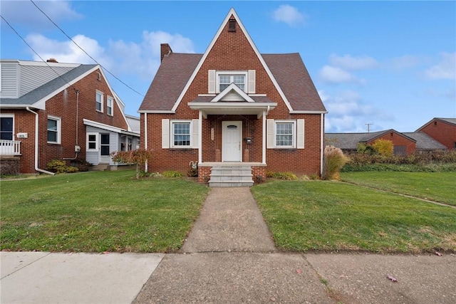 view of front facade with brick siding, a front yard, and a chimney
