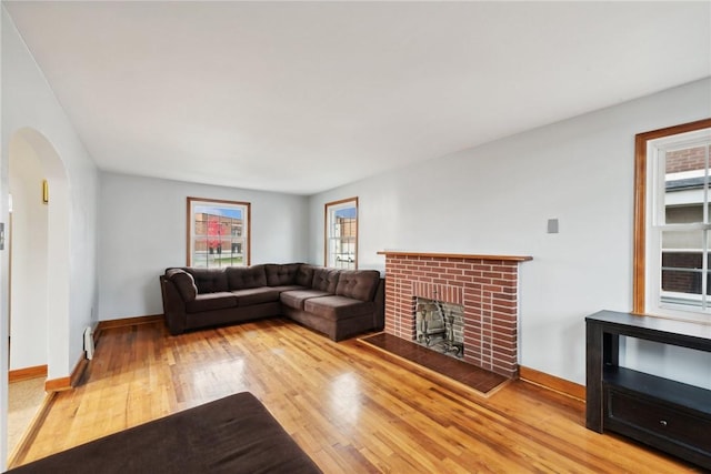 living area with wood finished floors, arched walkways, baseboards, and a brick fireplace