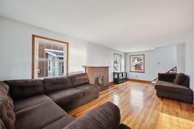 living room with light wood-style floors, stairway, a brick fireplace, and baseboards