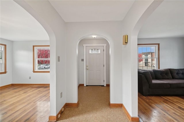 foyer featuring arched walkways, baseboards, and wood finished floors