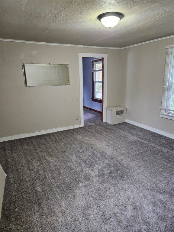 empty room featuring plenty of natural light, a textured ceiling, dark carpet, and ornamental molding