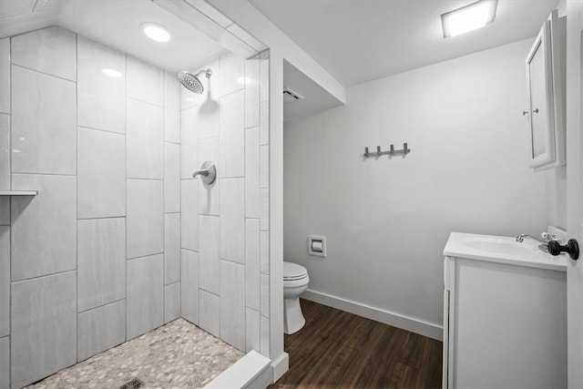 bathroom with a tile shower, hardwood / wood-style floors, vanity, toilet, and vaulted ceiling