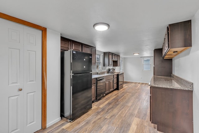 kitchen with appliances with stainless steel finishes, dark brown cabinets, light stone countertops, sink, and hardwood / wood-style flooring