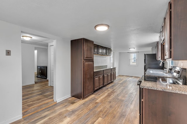 kitchen with dark wood-type flooring, light stone countertops, dark brown cabinets, and fridge