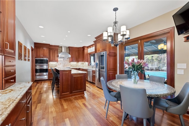 kitchen featuring wall chimney exhaust hood, light hardwood / wood-style flooring, a kitchen island, appliances with stainless steel finishes, and decorative light fixtures